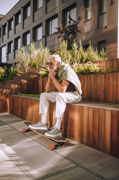 Male skateboarder with his feet on the skateboard sitting outside - Fotografie, Obrázek