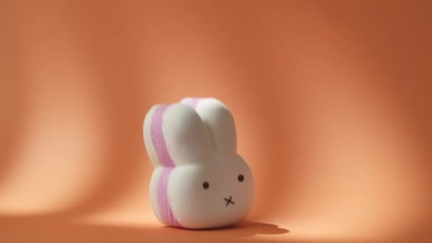 Büyük Beyaz ve Pembe Süngerli Tavşan turuncu arka plana düşüyorlar. Tavşan şekilli yumuşak oyuncak ağır çekimde turuncu yüzeyden sekiyor. 500 fps - Video, Çekim