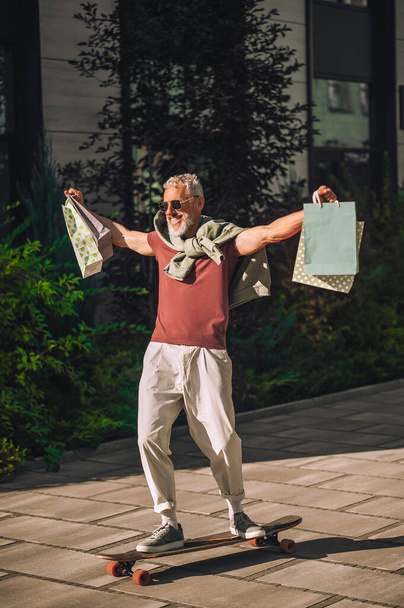 Cheerful skateboarder with shopping bags balancing on the board - Foto, imagen