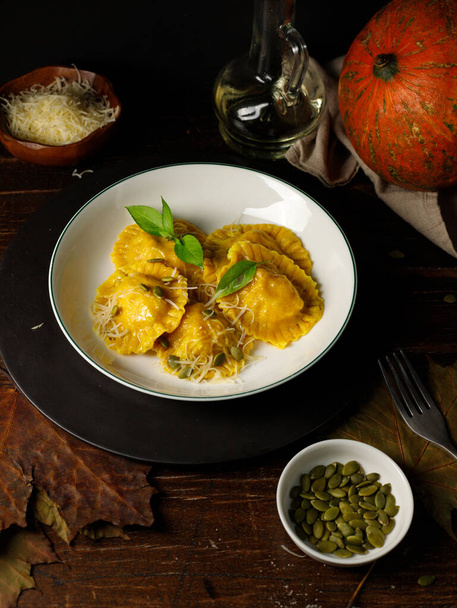 Pumpkin ravioli with ricotta and parmesan, decorated with seeds and basil. On a dark wooden table, a vertical, low key. - Photo, Image