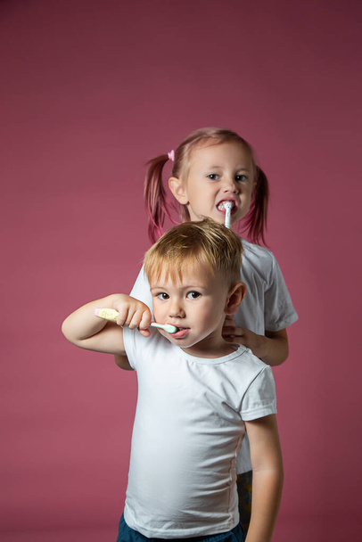 Smiling caucasian little boy and girl cleaning his teeth with electric sonic and manual toothbrush on pink background. - 写真・画像