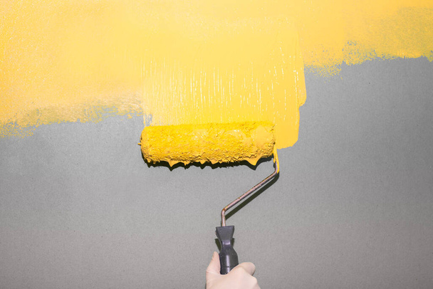 A painter rolls a bright yellow paint onto a gray wall background. Room painting. Pantone colors. - Valokuva, kuva