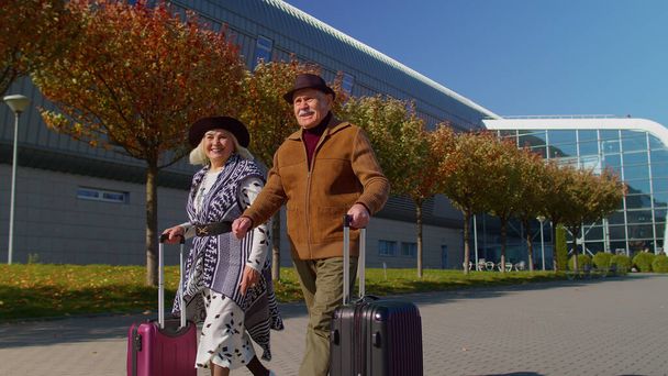 高齢者の夫の妻退職者の観光客は、車輪の上の荷物で搭乗するための空港ターミナルに行きます - 写真・画像