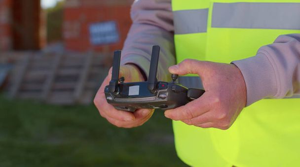 Drone operator holding remote controller controls an aircraft in front of construction house site - Photo, Image