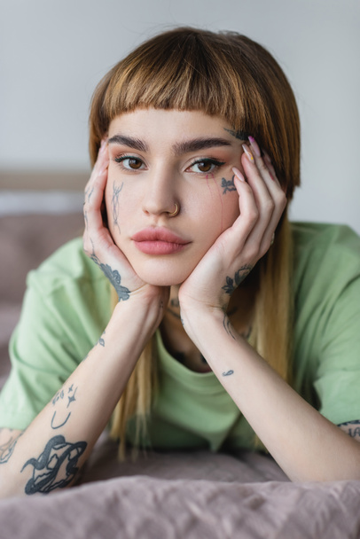 pretty young woman with tattooed face and hands looking at camera at home - Photo, Image