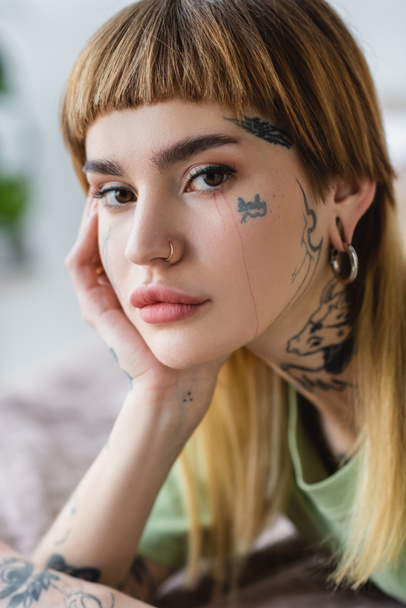 close up view of pretty woman with tattoo and piercing looking at camera at home - Fotó, kép