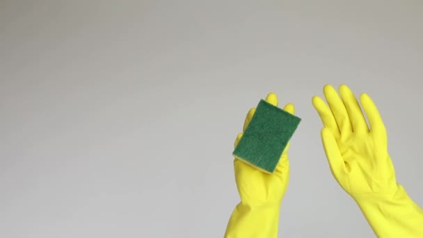 Mano de mujer en guante de goma protector amarillo y esponja de limpieza sobre fondo blanco. Vídeo 4k con espacio de copia para concepto de limpieza de texto o publicidad - Metraje, vídeo
