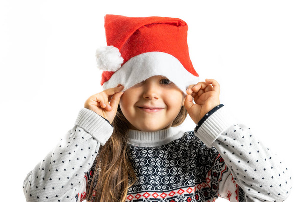 portrait of girl in white knitted Christmas sweater with reindeer hiding half face in Santa Claus hat, isolated on white background - Фото, изображение