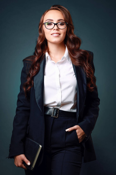 A beautiful middle-aged brunette woman in glasses and a business suit smiles and looks straight into the camera. - Φωτογραφία, εικόνα