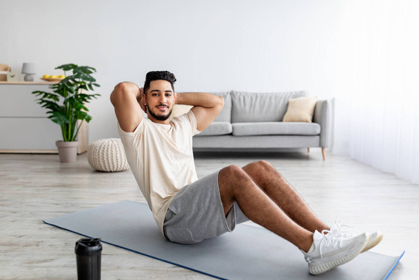 Sportowe tysiąclecie Arab człowiek robi ćwiczenia brzucha, ćwiczy w domu, pełna długość - Zdjęcie, obraz