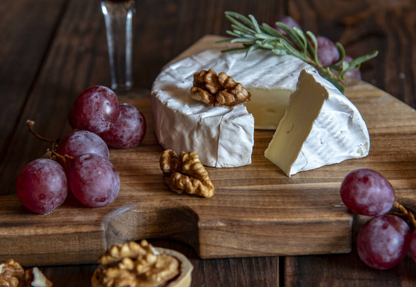 Cheese with white mold, nuts and grapes on a wooden cutting board. Food background. - Foto, Imagem