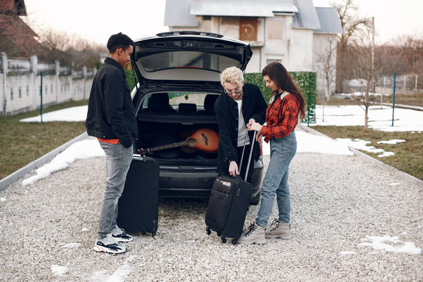 Two men and woman putting suitcases in a car - Foto, immagini