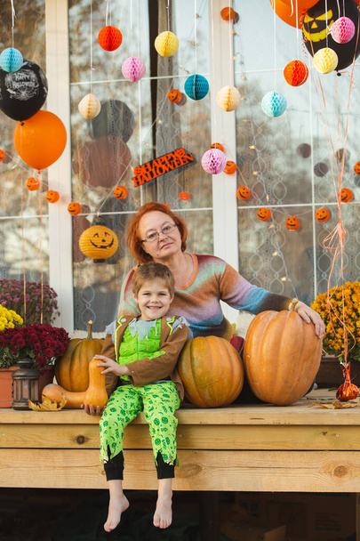 Als Zombie verkleideter kleiner Junge und seine Oma spielen auf der Terrasse ihres Hauses. Der Raum ist mit Themen-Luftballons, Girlanden, Chrysanthemen dekoriert. - Foto, Bild