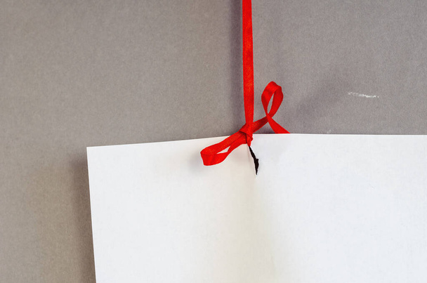 White sheet of paper and red ribbon against a gray background. Tied a blank sheet of paper vertically. Selective Focus. - Foto, imagen
