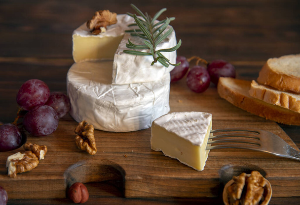 Cheese with white mold, nuts and grapes on a wooden cutting board. Food background. - Valokuva, kuva