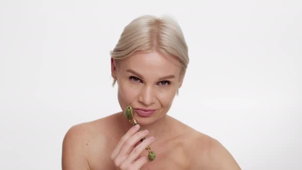 Bella donna di mezza età che utilizza il rullo facciale di giada di Greenstone per la cura della pelle - Filmati, video