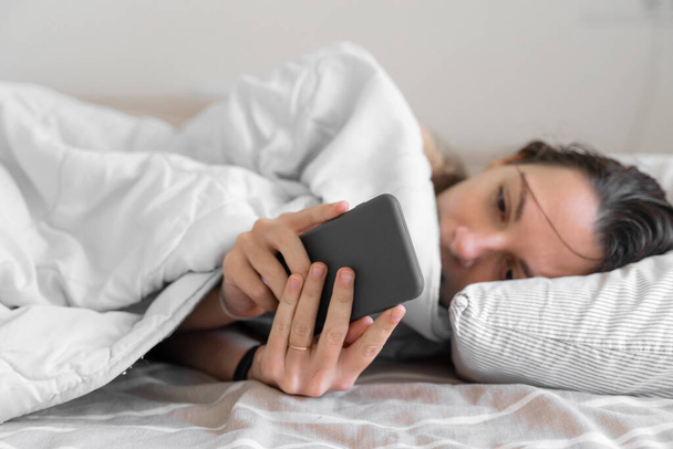 Young woman goes to sleep Phone addiction, insomnia. try to fall asleep. Sleep tracking on the phone. Circadian rhythm. - Φωτογραφία, εικόνα