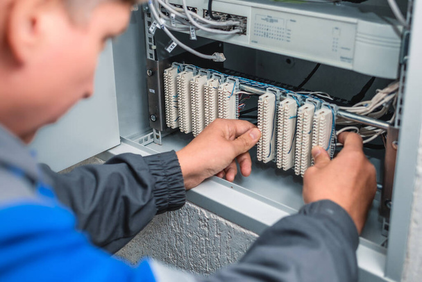 A man electrician checks the terminals of telephone communication equipment. - Foto, imagen