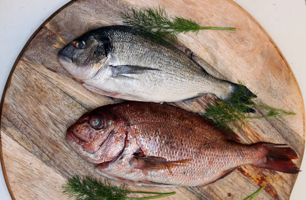 Frischer Fisch auf einem Holzschneidebrett. Ungekochter Dorada-Fisch auf einem Tisch. Konzept der gesunden Ernährung.  - Foto, Bild