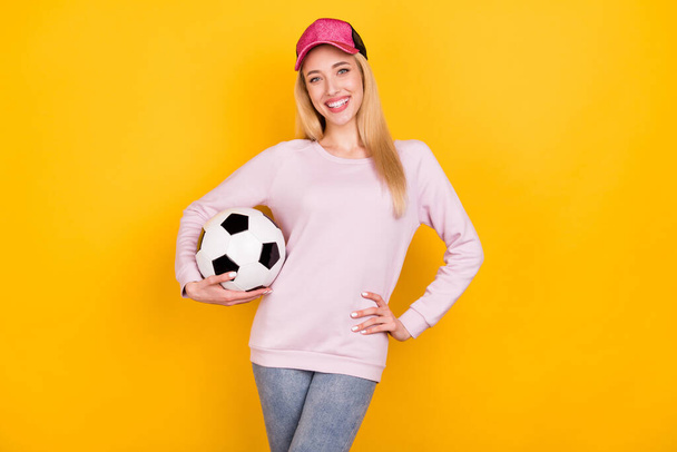 Photo portrait smiling woman in cap keeping soccer ball isolated bright yellow color background - Foto, Imagem
