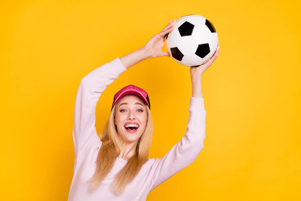 Photo portrait amazed woman in cap catching soccer ball laughing isolated bright yellow color background - Fotó, kép
