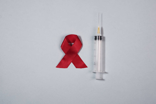 Clean syringe and red ribbon bow as symbol of AIDS and HIV awareness day - Фото, зображення