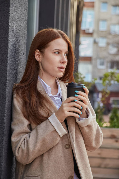 красива молода біла жінка в стильному бежевому пальто п'є каву на відкритому повітрі
 - Фото, зображення