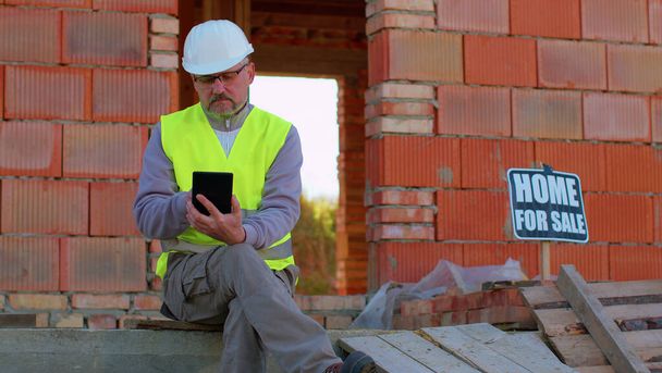 Архитектор с цифровым планшетным компьютером на строительной площадке, анализирующий чертежи здания - Фото, изображение