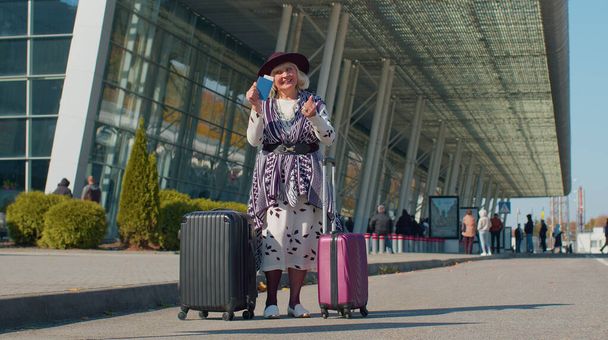 Старша пенсіонерка-туристична бабуся залишається біля залу аеропорту святкувати успіх жест переможця
 - Фото, зображення