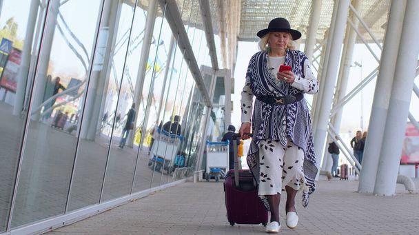 国際空港ホールを歩くシニア観光祖母の女性,携帯電話を使用して,テキストメッセージ - 写真・画像