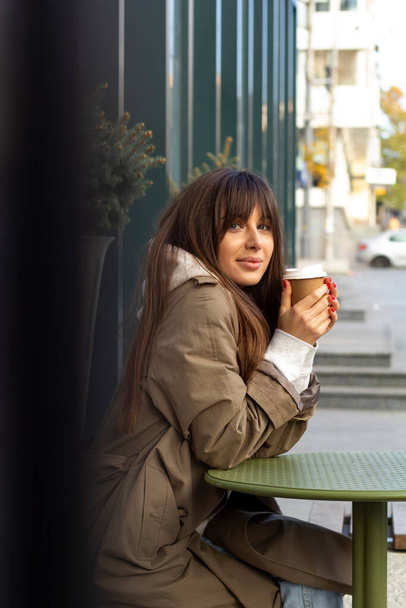 Young woman student drinks coffee in a cafe on a city street. - Foto, Bild