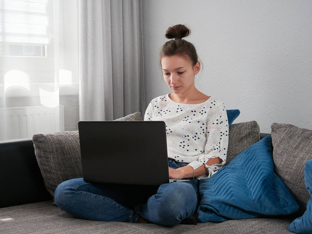 Oturma odasındaki kanepede oturan genç bir kadın bir dizüstü bilgisayar kullanıyor. Evdeki bilgisayarın önünde çalışıyorum.. - Fotoğraf, Görsel