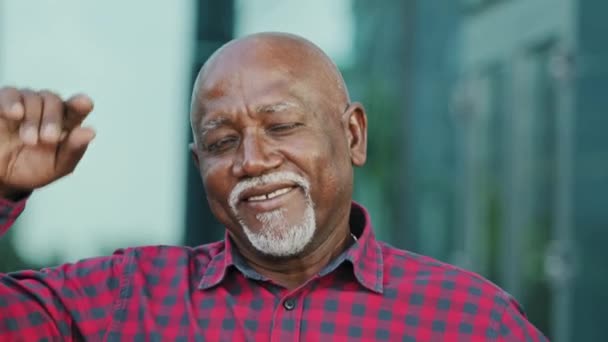 Portrait of positive elderly African American man with gray beard look at camera make video call wave hand welcome dialogue partner. Smiling adult person of retirement age invites, advertises services - Footage, Video