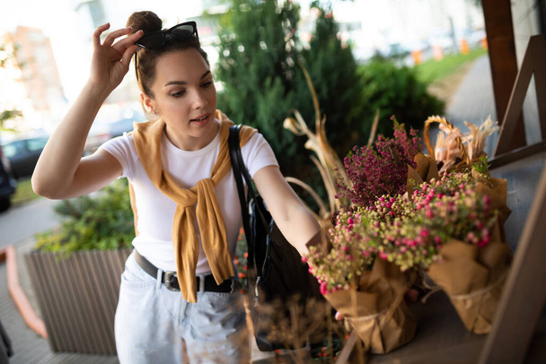 young beautiful brunette woman enjoying flowers in pots on the porch of a flower shop - Photo, Image
