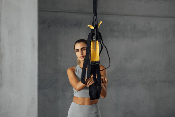 Кросфіт жінка стоїть в спортзалі, тримаючи фітнес-ремені в спортзалі
. - Фото, зображення