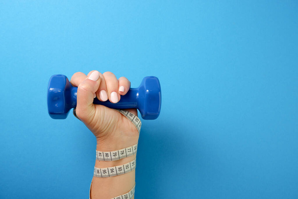 Sports concept. A woman's hand, wrapped with a measuring tape, holds a plastic dumbbell. - 写真・画像