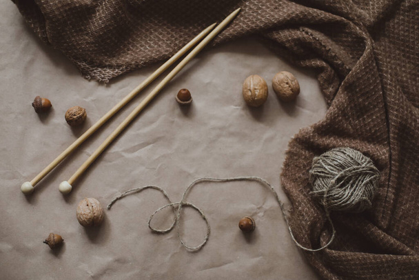 autumn and winter theme, brown paper texture background with cozy warm plaid, yarn and knitting needles, walnuts and acorns, top view, copyspace - 写真・画像