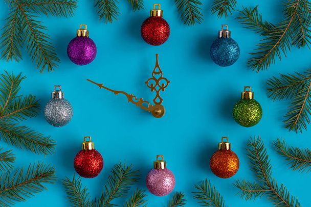 Diseño de moda con agujas de reloj, bolas de Navidad y ramas de un árbol de Navidad sobre un fondo azul. La Navidad de Año Nuevo y celebran los conceptos de fiesta. Tarjeta de felicitación. Fondo plano. - Foto, Imagen