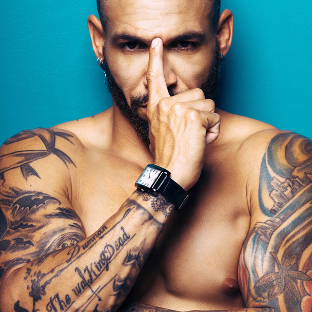 Studio portrait swarthy tanned man with a muscular body and tattoos looks directly into the camera. - Photo, Image