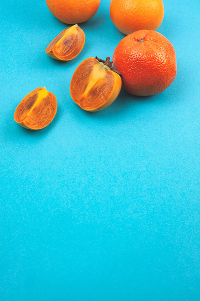 Juicy cut fruit oranges and persimmons on a trending blue background. - Foto, afbeelding