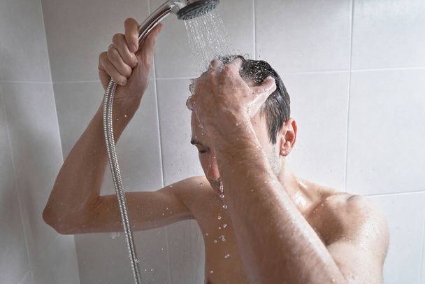 Portrait of young handsome man washes himself with shower gel, lathers head with shampoo in the bathroom at home close-up - Fotoğraf, Görsel