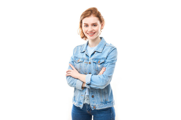 Portrait of a young red-haired girl on a white isolated background in jeans. Looks into the camera - 写真・画像