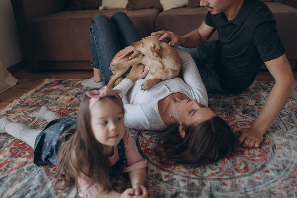 Νεαρή οικογένεια στο σαλόνι παίζει με ένα σκυλί  - Φωτογραφία, εικόνα