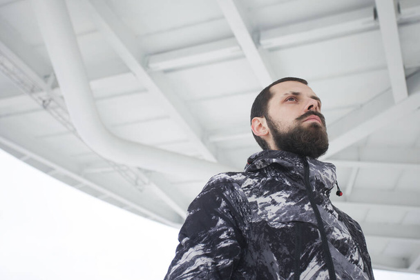 Winter weather clothing concept. Close up portrait of brutal bearded charismatic 30-year-old man standing over futuristic background. Stylish haircut. Copy-space. Outdoor shot - Photo, image