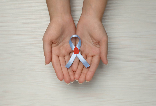 Woman holding light blue ribbon with paper blood drop at wooden table, top view. Diabetes awareness - Foto, immagini