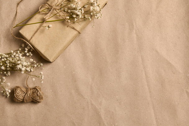 Composition vue grand angle avec tige de gypsophila blanche sur boîte cadeau en papier kraft et nœud de corde attaché au coin d'un fond en carton froissé avec espace de copie pour la publicité - Photo, image