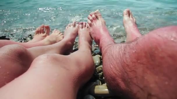 Estos son los pies desnudos de una familia en las olas del mar en una orilla de piedra.  - Metraje, vídeo