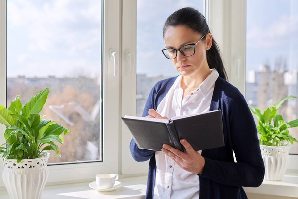 Adult woman with notepad and pencil at home near the window - Photo, Image