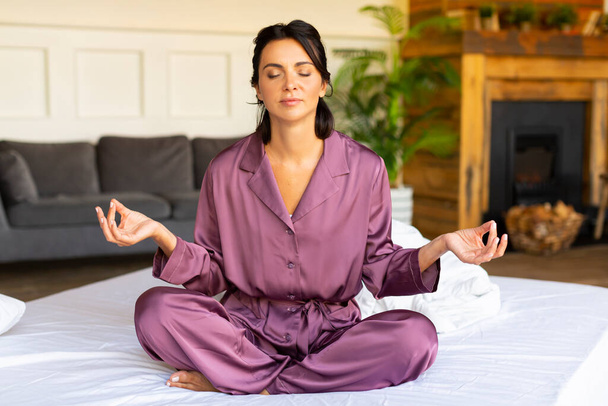 Привлекательная женщина средних лет медитирует на кровати. Малое здоровье и цифровая детокс-концепция. - Фото, изображение
