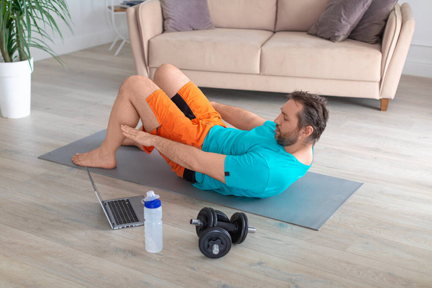 ABS workout in front of a laptop monitor. Man looks at the monitor and trains with an online guide. - Photo, Image